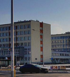 Budynek z oknami i pomarańczowymi pasami, samochód na ulicy. Kontekst miejski, dzień.
