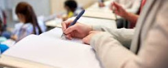 Osoba pisze w notatniku podczas wykładu. W tle inni studenci siedzą w amfiteatrze.