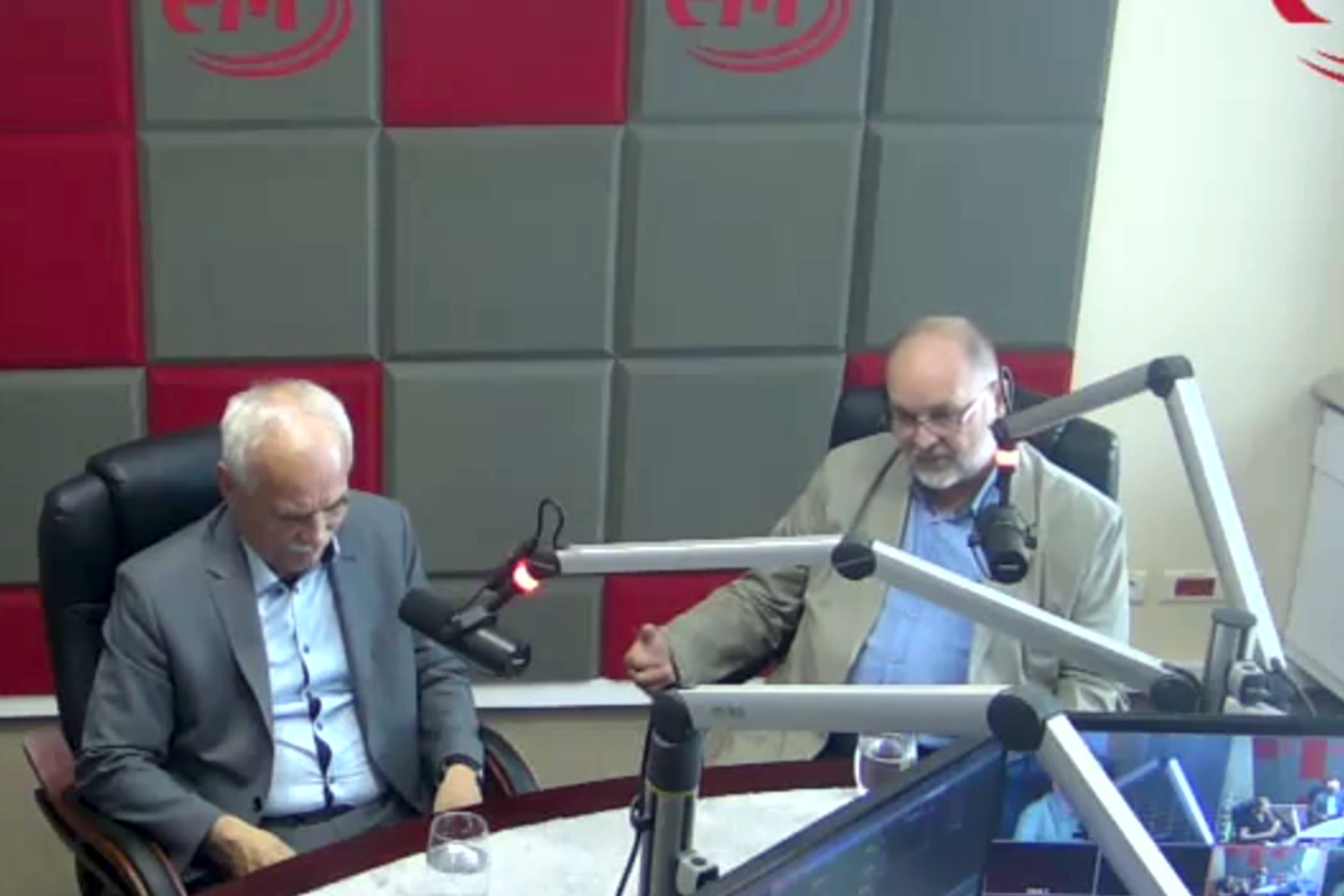 Dwóch mężczyzn w studiu radiowym przy mikrofonach. Mężczyźni siedzą przy stole, rozmawiają.