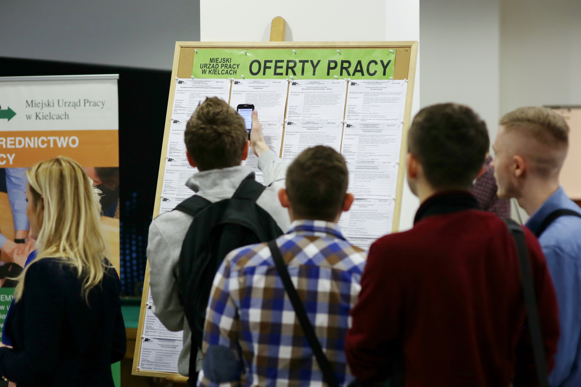 Tablica z ofertami pracy Miejskiego Urzędu Pracy w Kielcach. Ludzie przeglądają ogłoszenia.