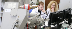 Dwoje naukowców w białych fartuchach pracuje przy skomplikowanej aparaturze laboratoryjnej i monitorach.