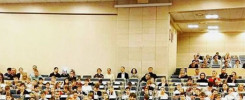 Widownia pełna dzieci i dorosłych siedzących w rzędach. Konferencja lub wydarzenie szkolne.